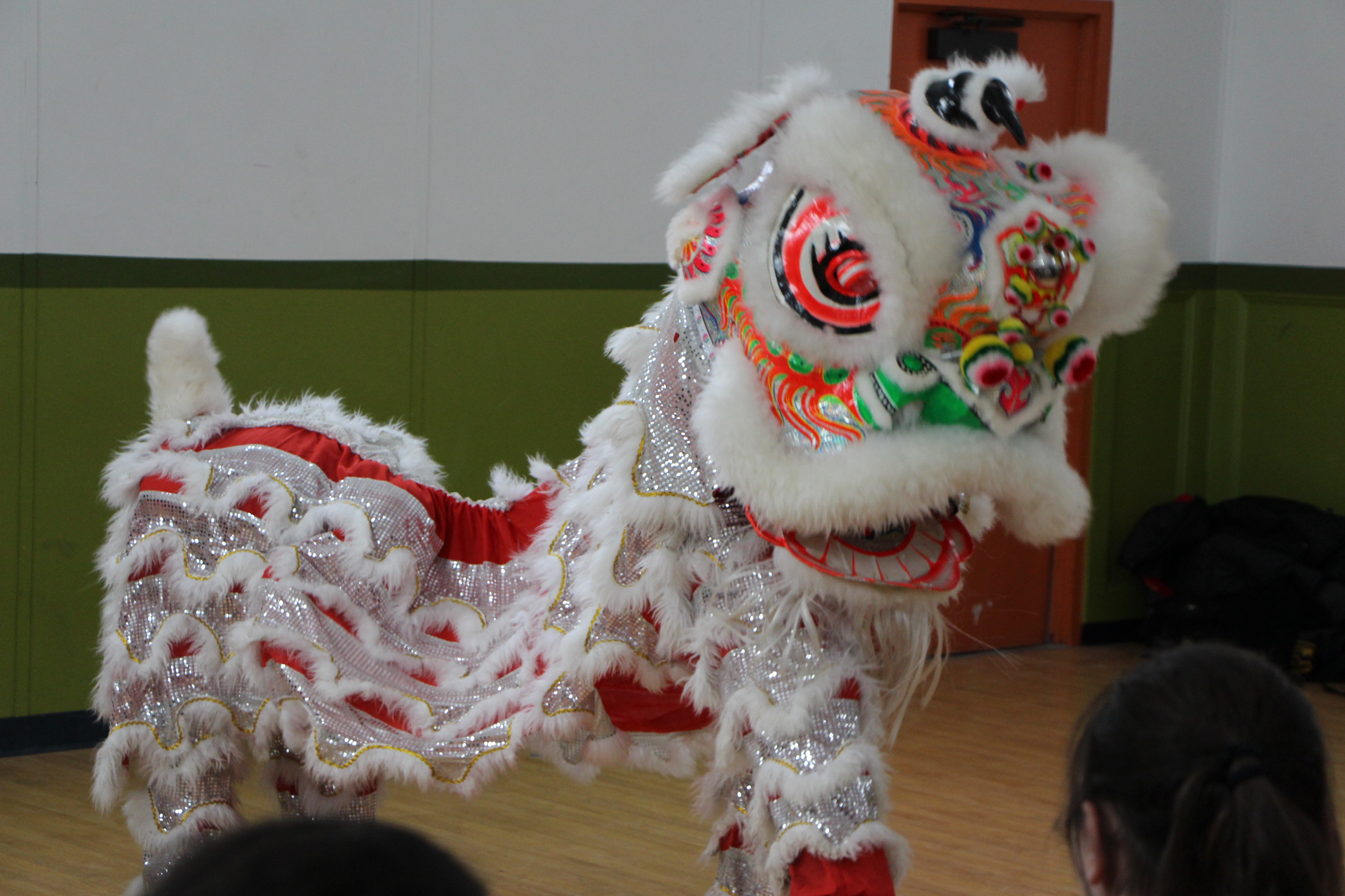 Two performers in a traditional Chinese lion costume perform for students