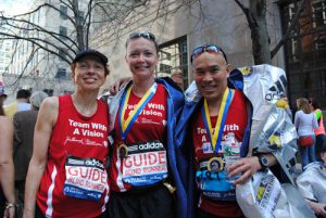 Team With A Vision runner John Chan poses with his two female sighted guides, all wearing Team With A Vision shrts, pose after running the Boston Marathon