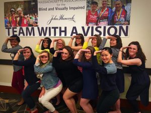 Delta Gamma sisters give the DG salute in front of a MABVI Team With A Vision banner