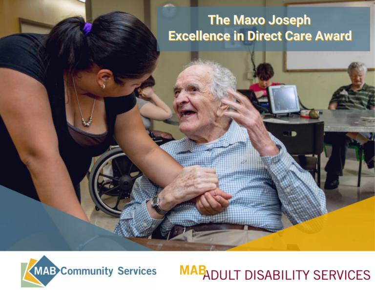 Direct care worker holding the hand of a man in a wheelchair who is looking up and smiling