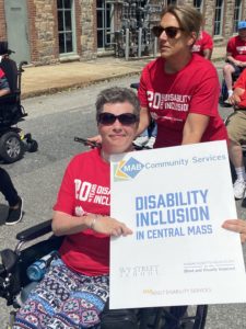 Image of woman in wheelchair holding a sign that says disability Inclusion in Central Mass 