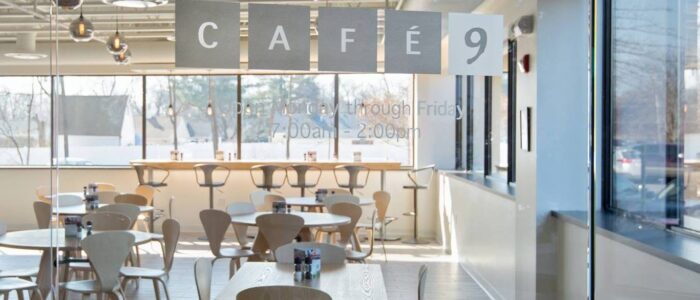 A brightly lit cafe dining area with a sign that has the words CAFE 9 on it and a window in the background.