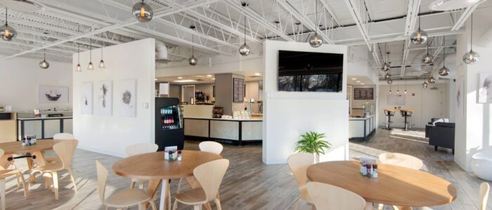 A brightly lit cafe seating area with light colored furniture and an ordering are in the background.